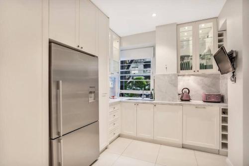 a kitchen with white cabinets and a stainless steel refrigerator at Henrietta's Gem - Close to cafes, shops and more in Sydney