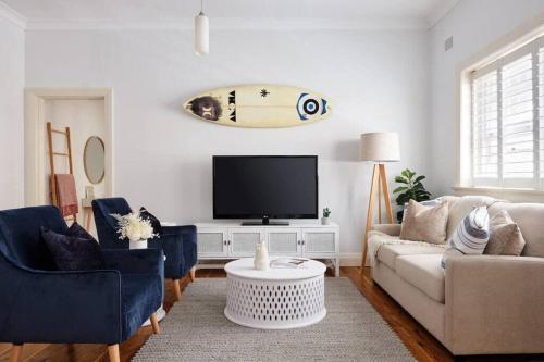 a living room with a couch and a surfboard on the wall at Edward Escape - Short Walk to Beach in Sydney