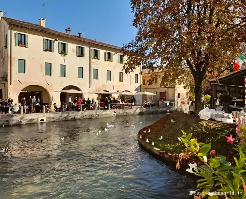 a river with people sitting at tables next to a building at Ca' Molinetto in Treviso