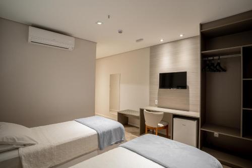a hotel room with two beds and a desk and a tv at Zahara Hotel in Limeira