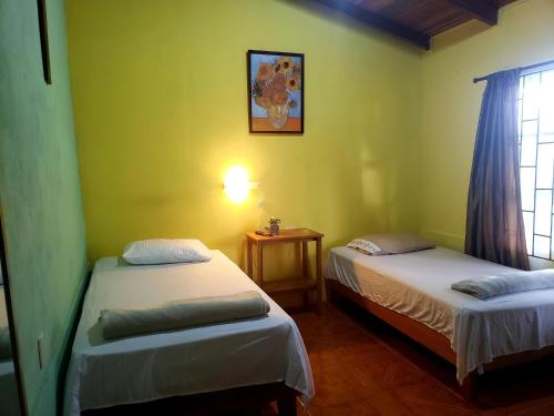 two beds in a room with yellow walls and a window at Arenal Hostel La Catarata in Fortuna