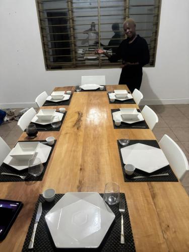 Ein Mann steht vor einem Holztisch mit Stühlen. in der Unterkunft White House -Two palms in Kampala