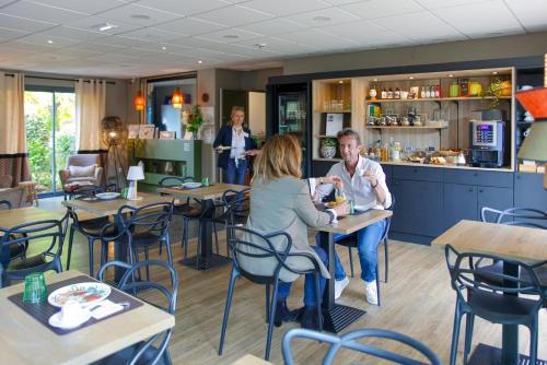 un hombre y una mujer sentados en una mesa en un restaurante en Hôtel & Events LE PATIO OCCITAN Toulouse Ouest - Cugnaux, en Cugnaux