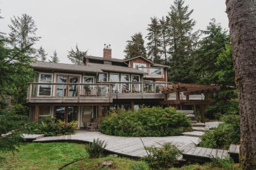 a house with a wrap around deck in the woods at Chesterman on the Point - Beachfront in Tofino