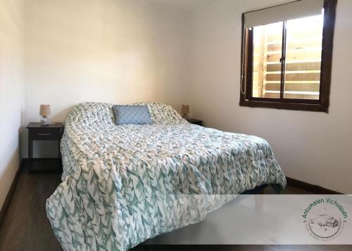 a bedroom with a bed with a comforter and a window at Cabañas Antumalen Vichuquén in Lago Vichuquen