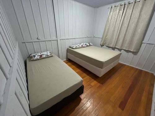 two beds in a small room with wooden floors at Casa Átrio em Biguaçu próximo às Praias in Biguaçu