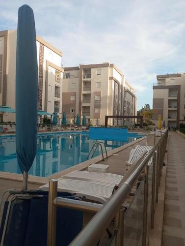 a swimming pool with a blue umbrella and some chairs at Appartement Neuf au Bord de la Mer - Hammamet Sud Zone Touristique in Hammamet