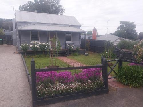 a fence in front of a house with purple flowers at Lavender Cottage - Cute & Cosy Miner's Cottage in Ballarat