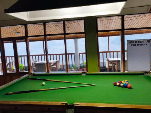 Una mesa de billar frente a una habitación con ventanas. en Hotel BHRIGU, en Manali