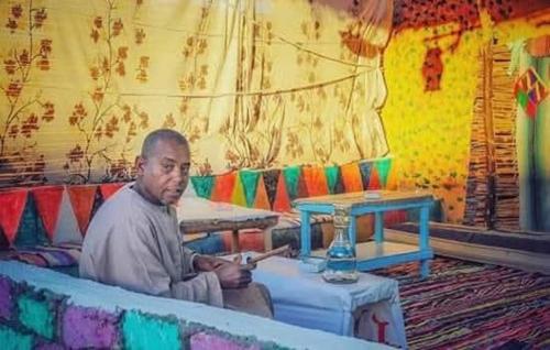 Jazīrat FīlahShamandora Nubian Guest House的坐在房间长凳上的男人
