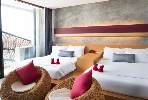 two beds with red pillows and chairs in a room at The Now Hotel - SHA Extra Plus in Jomtien Beach