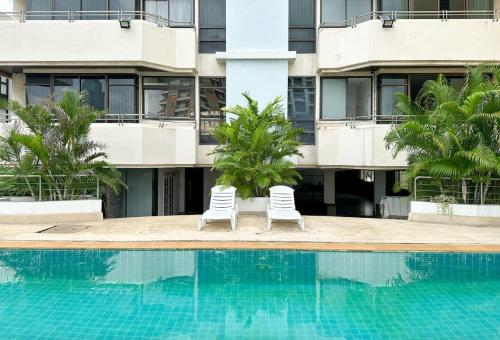 two white chairs next to a swimming pool in front of a building at Cozy, Spacious 2-Bedder with City, Park View, Near Nana BTS in Bangkok