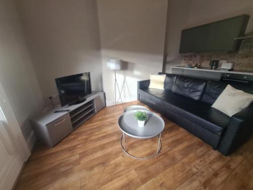 a living room with a black couch and a table at Tyneside Apartments 5 Minutes From City Centre in Newcastle upon Tyne