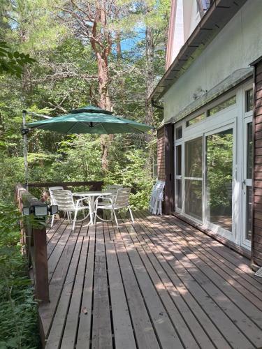 a wooden deck with a table and an umbrella at Mountain chalet getaway at Fuji-Sanroku 富士山麓のシャレー風山荘 in Narusawa