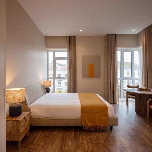 a bedroom with a bed and a desk and windows at Foz Apartments & Suites in Figueira da Foz