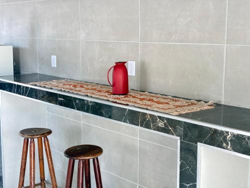 Eine rote Vase steht auf einer Theke mit zwei Hockern. in der Unterkunft Pousada sussego in Prado