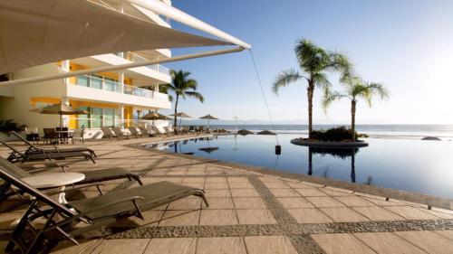 a resort with a pool with chairs and palm trees at Condo Vela Vista 1004 by Kivoya in Nuevo Vallarta