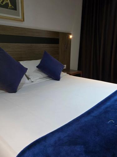 a large white bed with blue pillows on it at Tanger Med Hotel, Conference & Catering in Ghdar Defla