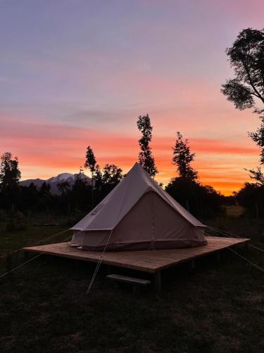 a tent in a field with a sunset in the background at Glamping Peumayen carpintero in Llanquihue