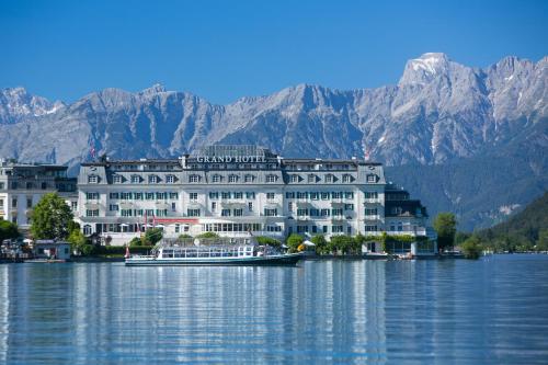 a large building on the water with mountains in the background at Grand Hotel Zell am See in Zell am See