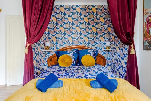 una camera da letto con un letto con lenzuola blu e gialle e tende rosse di Le Romantique - Place St Didier - Cœur de ville ad Avignone