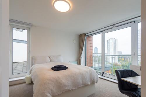 ein weißes Schlafzimmer mit einem Bett und großen Fenstern in der Unterkunft Modern High-Floor 3BR with Terrace & Thames View in Kew Bridge
