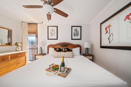 a bedroom with a white bed with a bottle of champagne at Paki Maui 217 · PM 217 Cozy 1BR Oceanfront Condo w Pool in Lahaina