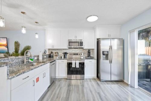 a kitchen with white cabinets and a stainless steel refrigerator at Stylish Townhome w Hot Tub 5 Min Walk to Beach in Cape Canaveral