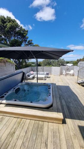 a hot tub on a wooden deck with an umbrella at Paradise on the Shore Auckland with large Spa Pool in Auckland
