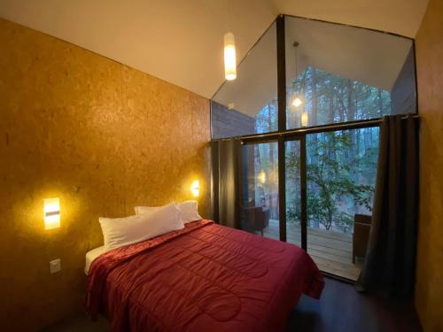 una camera con un letto rosso e una grande finestra di BosqueCielo Cabañas Diseño Natural Arte Galeria a Huasca de Ocampo