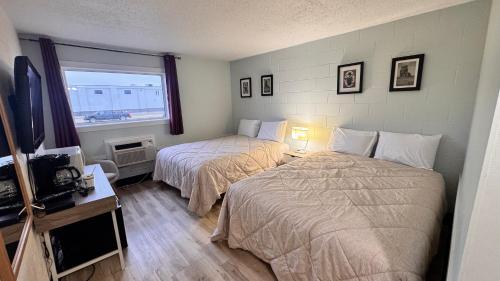 a bedroom with two beds and a tv and a window at Confederation Inn in Saskatoon