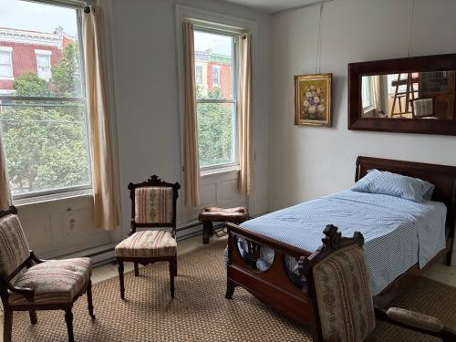 a bedroom with a bed and two chairs and windows at Gilded Age Tower in Philadelphia
