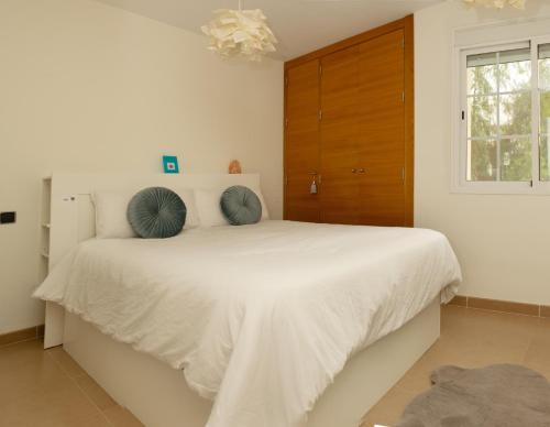 Un dormitorio blanco con una cama grande con almohadas azules. en Confortable apartamento con garaje en Aguadulce, en Roquetas de Mar