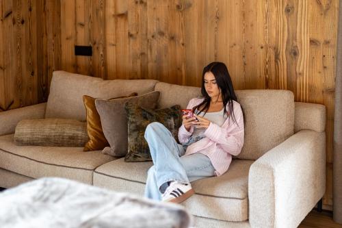 a woman sitting on a couch looking at her cell phone at Paradise Lodge in Livigno