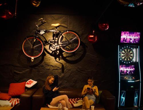 two women sitting on a couch with a bike on the wall at Bed Attitude Hostel Cenang in Pantai Cenang