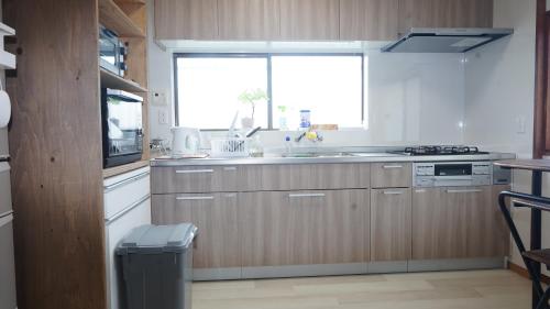 a kitchen with wooden cabinets and a sink and a window at PANARI guest house NISHIHONMACHI in Ube