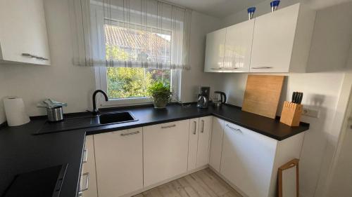 Ferienwohnung Lilienthal في Lilienthal: مطبخ بخزائن بيضاء وطاولة عمل سوداء