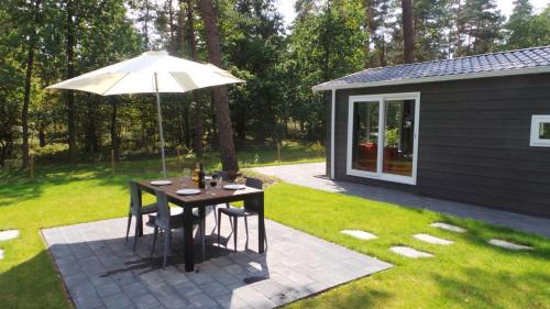 a table with an umbrella next to a cabin at Chalet de Bosrand 404, unieke rustige plek met veel privacy aan de bosrand van vakantiepark op de Veluwe in Beekbergen