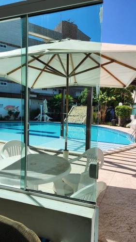 a white table and chairs under an umbrella next to a pool at Mandakaru Residence Flat da Isa 01 in Porto De Galinhas