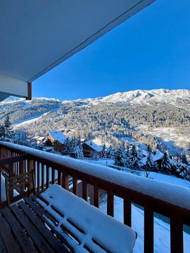 uma varanda coberta de neve com um banco e montanhas nevadas em Appartement 4 personnes - Magnifique vue montagne em Méribel