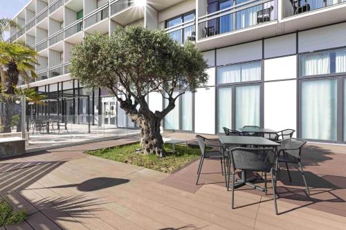 una mesa, sillas y un árbol frente a un edificio en B&B Hotel Savona, en Savona