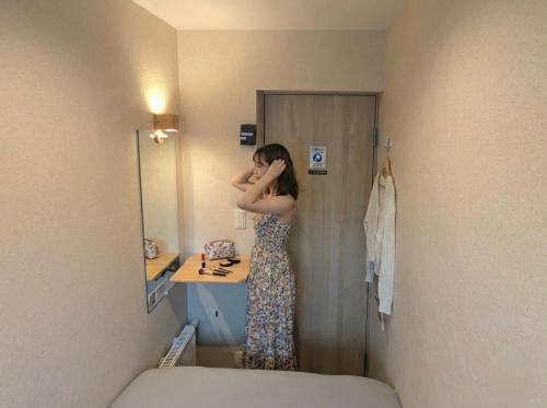 a woman standing in a bathroom in front of a mirror at Sho inn MINIMAL HOTEL 小樽駅から無料送迎あり in Otaru
