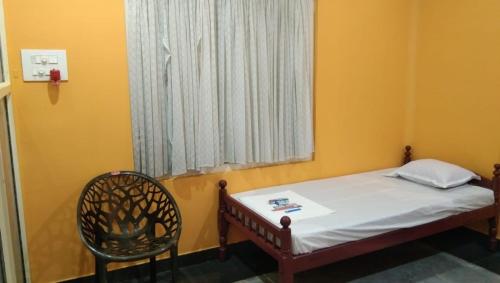 KunnamkulamCharis Guest house near Guruvayur, Kunnamkulam的一间卧室，里面有一张床、一把椅子和一扇窗户
