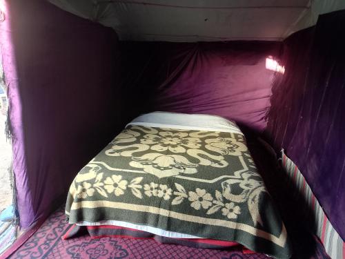 ein Bett in einem lila Zelt mit einer Decke in der Unterkunft Travel Oasis Merzouga Camp in Merzouga