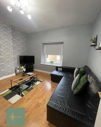 a living room with a black leather couch and a table at Orlando Llandundo Apartment in Llandudno