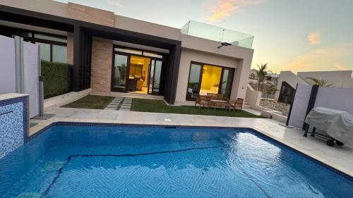 a swimming pool in front of a house at The Pearl villa sifah muscat in As Sīfah