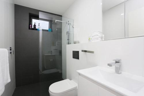 a white bathroom with a shower and a toilet at Hoffy's Place - Modern one bedroom with AC in Sydney