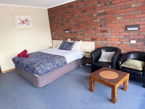 a bedroom with a bed and two chairs and a brick wall at Coorrabin Motor Inn in Stawell