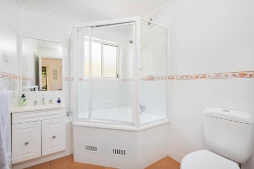 a white bathroom with a shower and a toilet at Coastal play and stay - walk to beach and park in Toowoon Bay