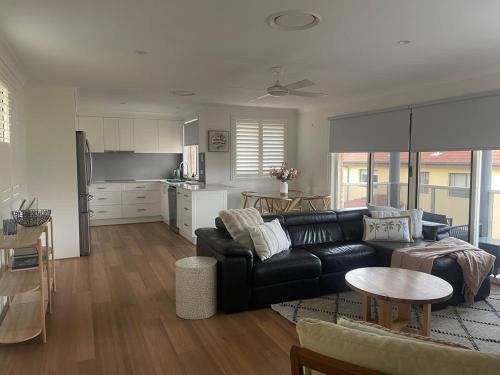 a living room with a black couch and a kitchen at Coastal play and stay - walk to beach and park in Toowoon Bay